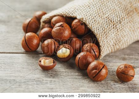 Macadamia Nuts Spilled Out Of The Bag On A Wooden Background Close-up With One Peeled Nut