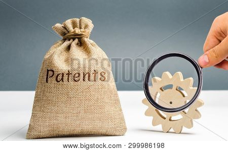 Money Bag With The Word Patents And A Wooden Gear. Registration Of Patents And Copyright Compliance.