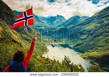 Female Tourist With Norwegian Flag Enjoying Scenic View Over Fjord Geirangerfjord With Cruise Ship. 
