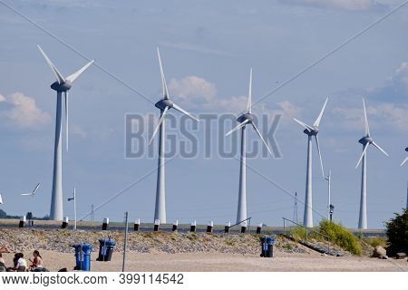 Urk, The Netherlands - June 15 2020 Windmills On The Coast With Rubbish Bins, People And Birds Movin