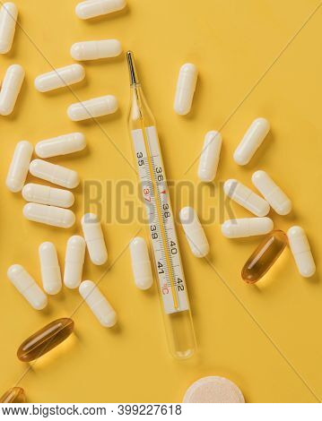 Thermometer And Pills. Top View On Isolated Yellow Background. Still Life