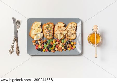 Four French Toast Slices Of Fruit, Nuts, And Granola On A Gray Rectangular Plate. Top View On A Whit
