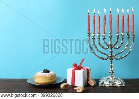 Silver Menorah Near Dreidels With He, Pe, Nun, Gimel Letters, Gift Box And Sufganiyah On Wooden Tabl