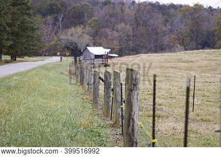 Wooden Posts Of A Barbed Wire Fence With Electric Wire Offset Leading To An Old Barn In The Distance