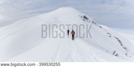 Senior Couple Is Snowshoe Hiking In Alpine Snow Winter Mountains Panorama. Allgau, Bavaria, Germany.