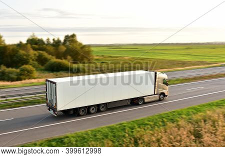Truck With Semi-trailer Driving Along Highway On The Blue Sky Background. Goods Delivery By Roads. S
