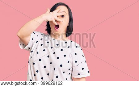 Brunette woman with down syndrome wearing casual clothes peeking in shock covering face and eyes with hand, looking through fingers with embarrassed expression. 