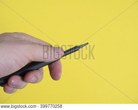 A Man's Hand Holds A Small Screwdriver With A Torx Nozzle On A Bright Yellow Background. Copy Space