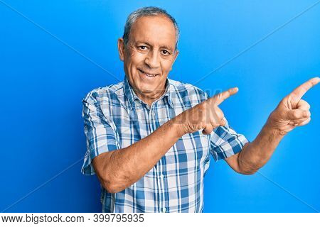 Senior hispanic man wearing casual clothes smiling and looking at the camera pointing with two hands and fingers to the side. 