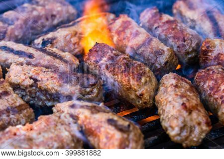 Preparing Meat Rolls Called Mici Or Mititei On Barbecue. Close Up Of Grill With Burning Fire With Fl