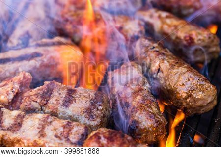Preparing Meat Rolls Called Mici Or Mititei On Barbecue. Close Up Of Grill With Burning Fire With Fl