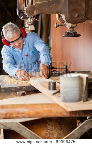 Senior carpenter using bandsaw to cut wood in workshop