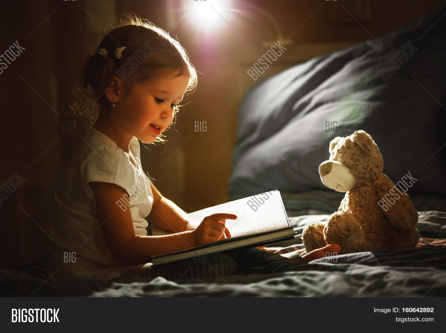 child girl reading a book in bed before going to sleep