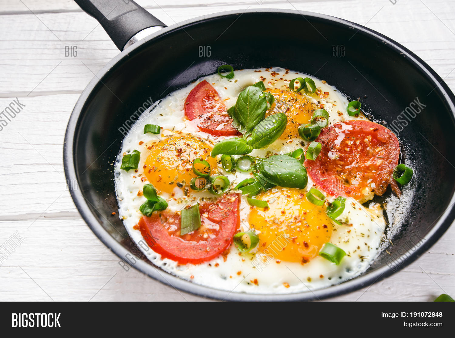 pan of fried eggs with tomatoes, cheese, spring onion, herbs on