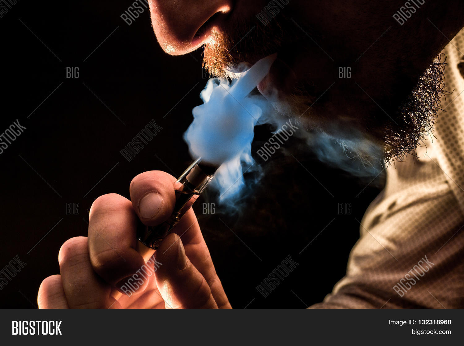 dramatic lighting bearded man smokes a vape e-cigarette