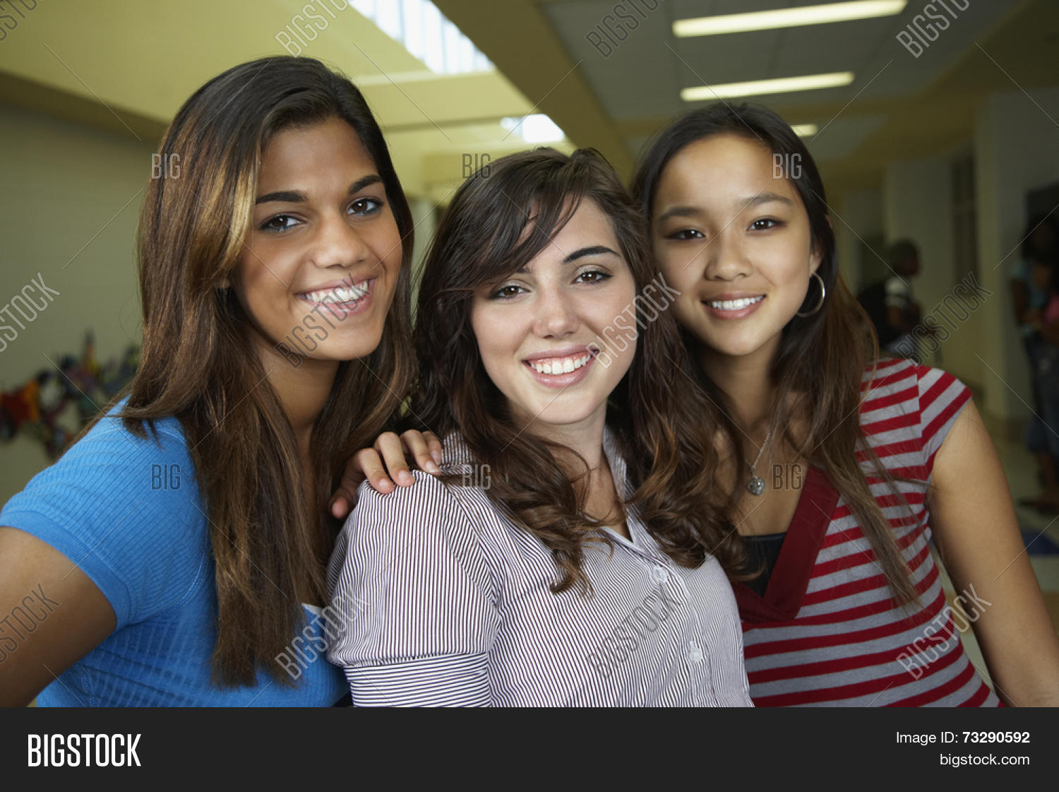 multi-ethnic teenaged girls hugging in school hallway