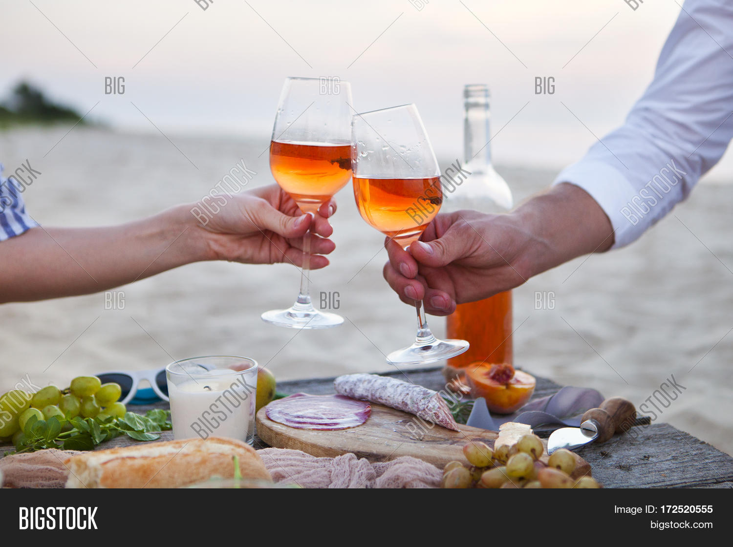 man and woman clanging wine glasses with rose wine at picnic