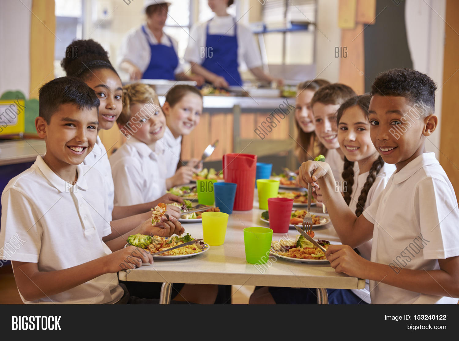 kids at a table in a primary school cafeteria look to camera