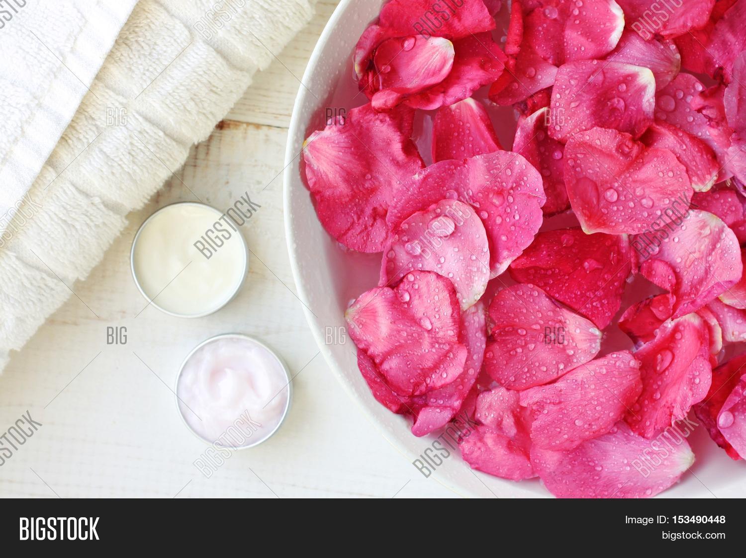 rose petals in bowl, body care moisturizers, white towel.