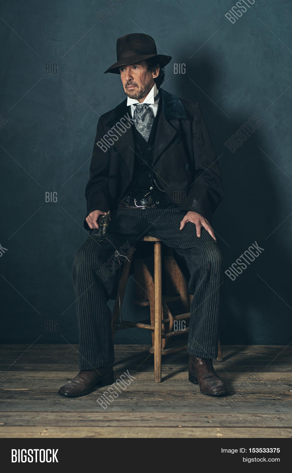 vintage 1900 western mature man with revolver sitting on wooden