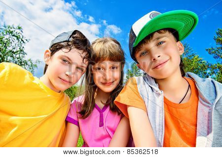 three joyful children looking at the camera against the blue sky