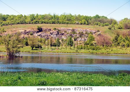 landscape of a green grassy hills, trees, river and sky