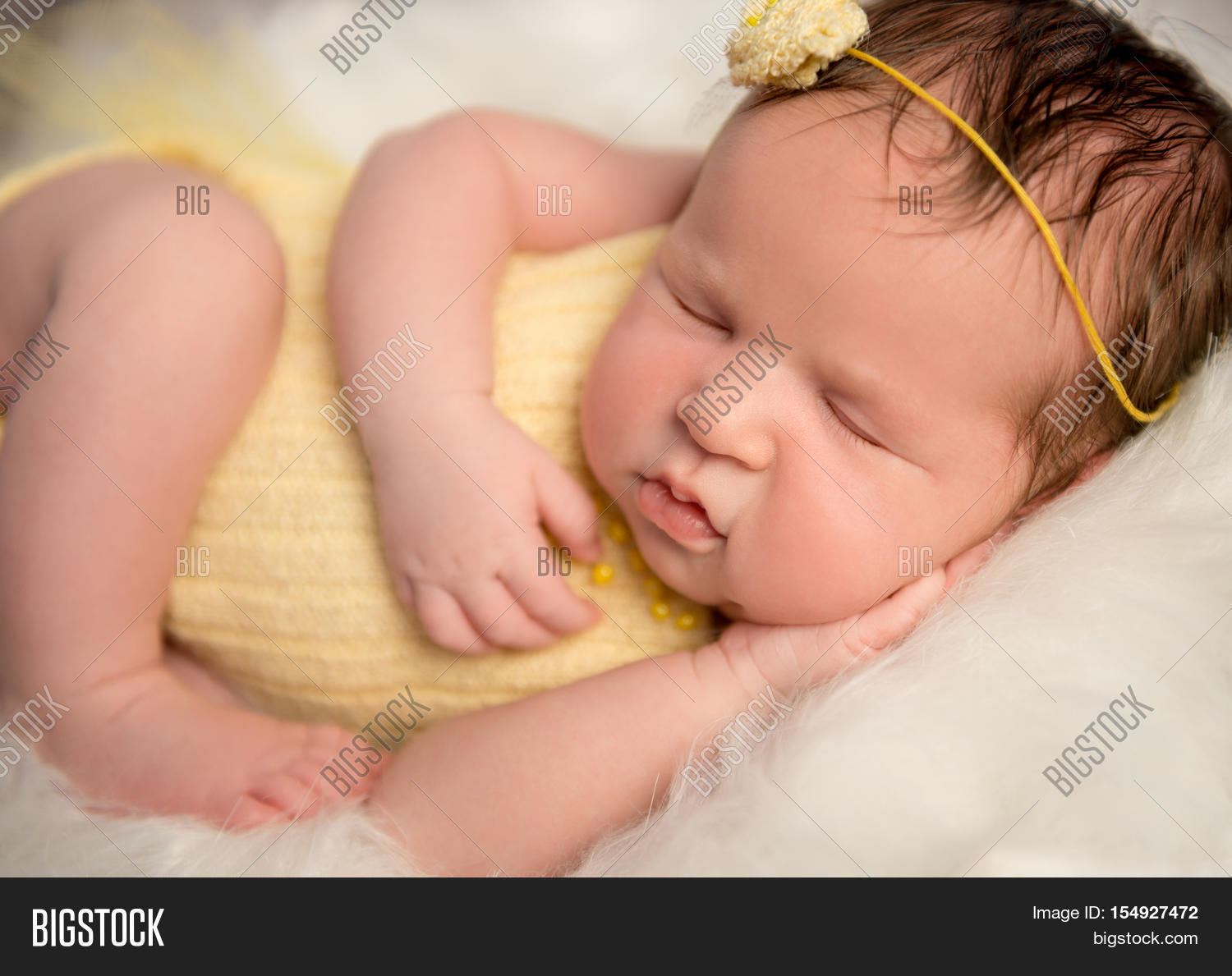 lovely newborn baby in yellow romper and headband sleeping with