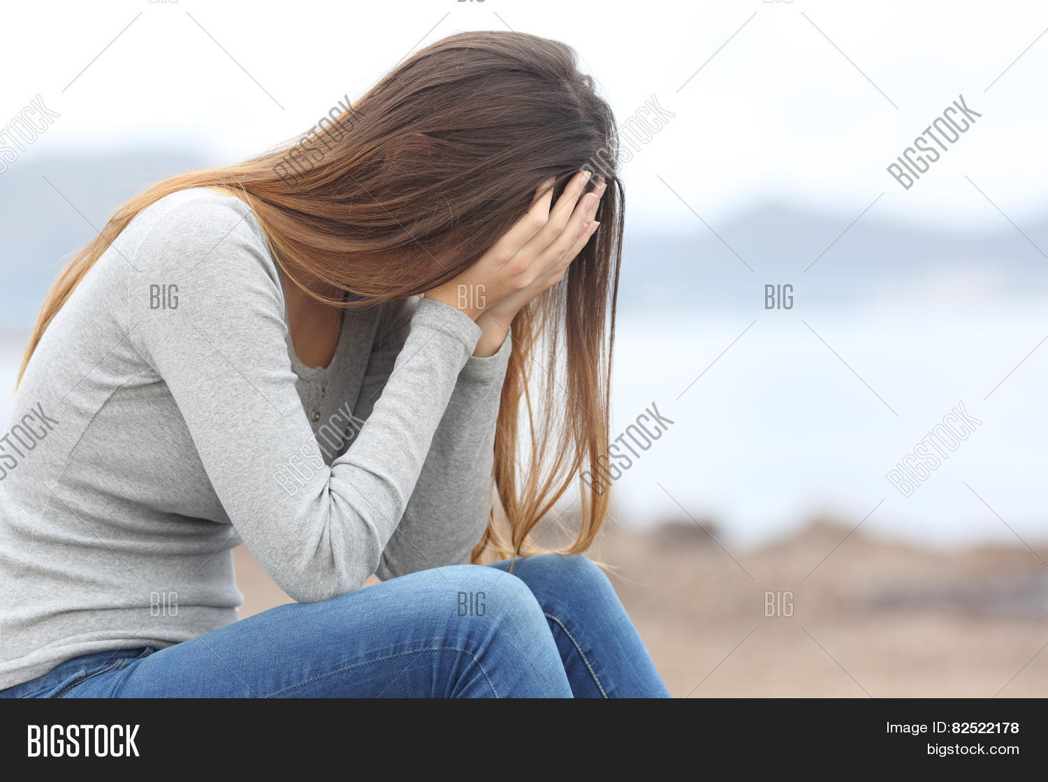 worried teenager woman covering her face with hands on the beach