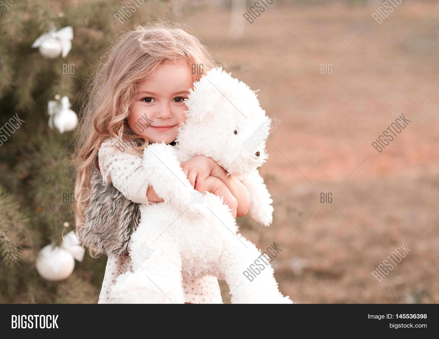 smiling baby girl 4-5 year old holding teddy bear outdoors.
