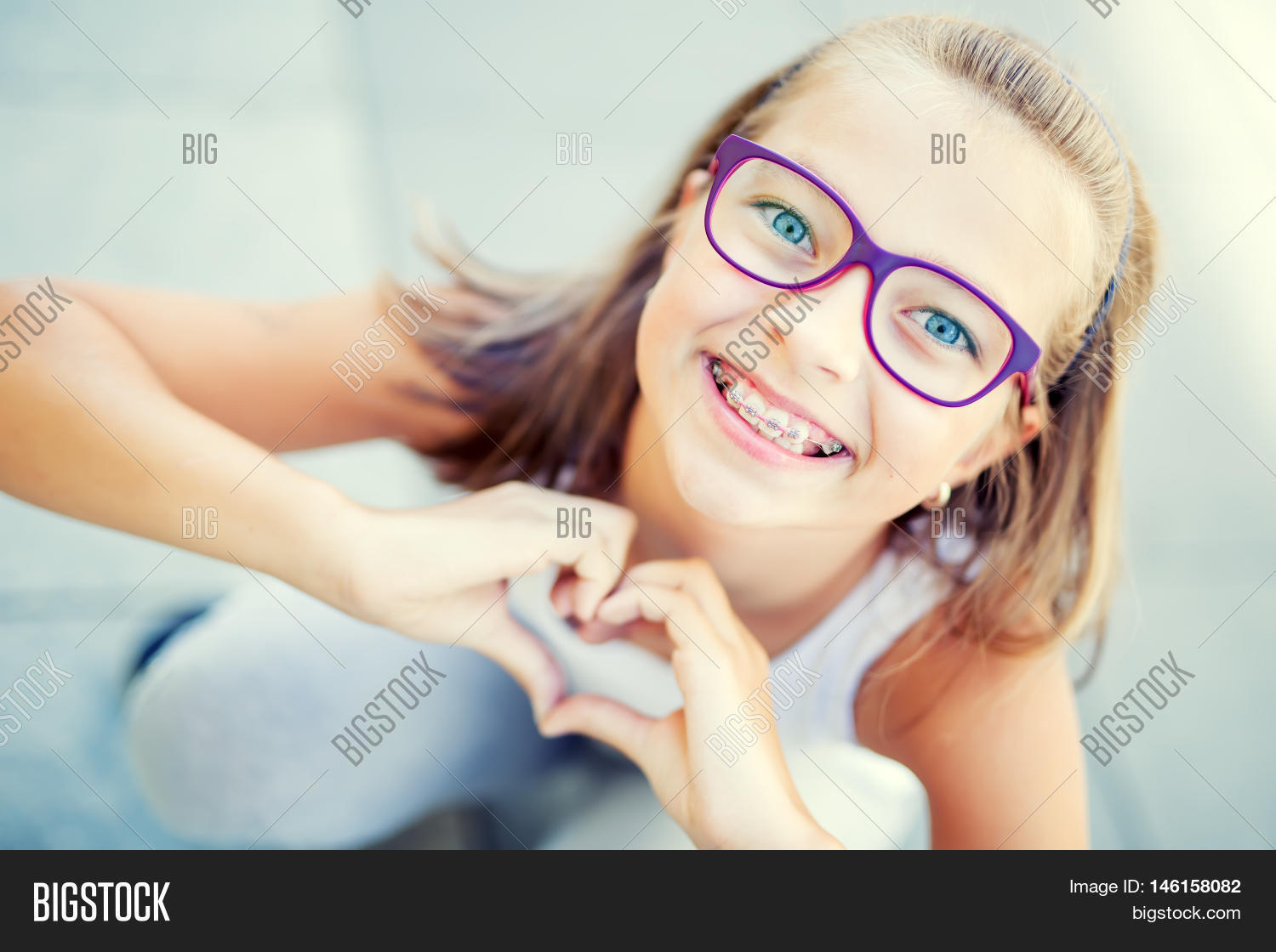 smiling little girl in with braces and glasses showing heart