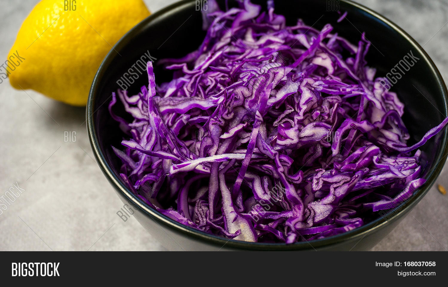 shredded red cabbage with lemon in black bowl on grey background