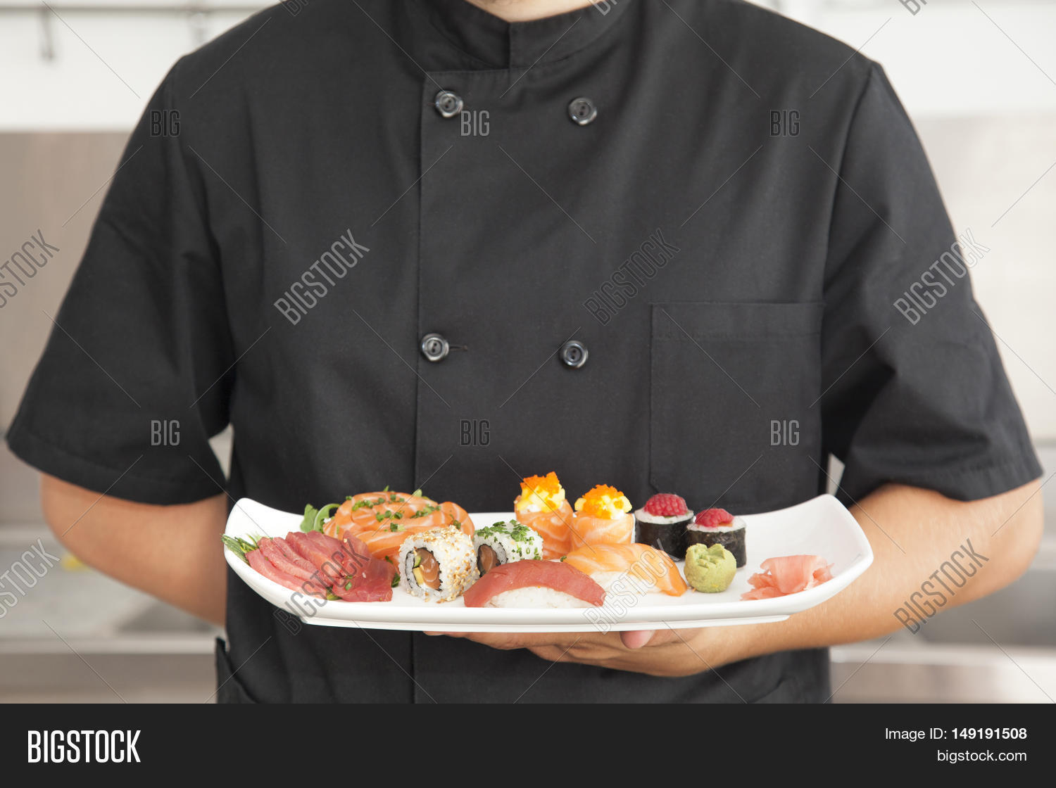 male chef holding a plate full of sushi at the kitchen